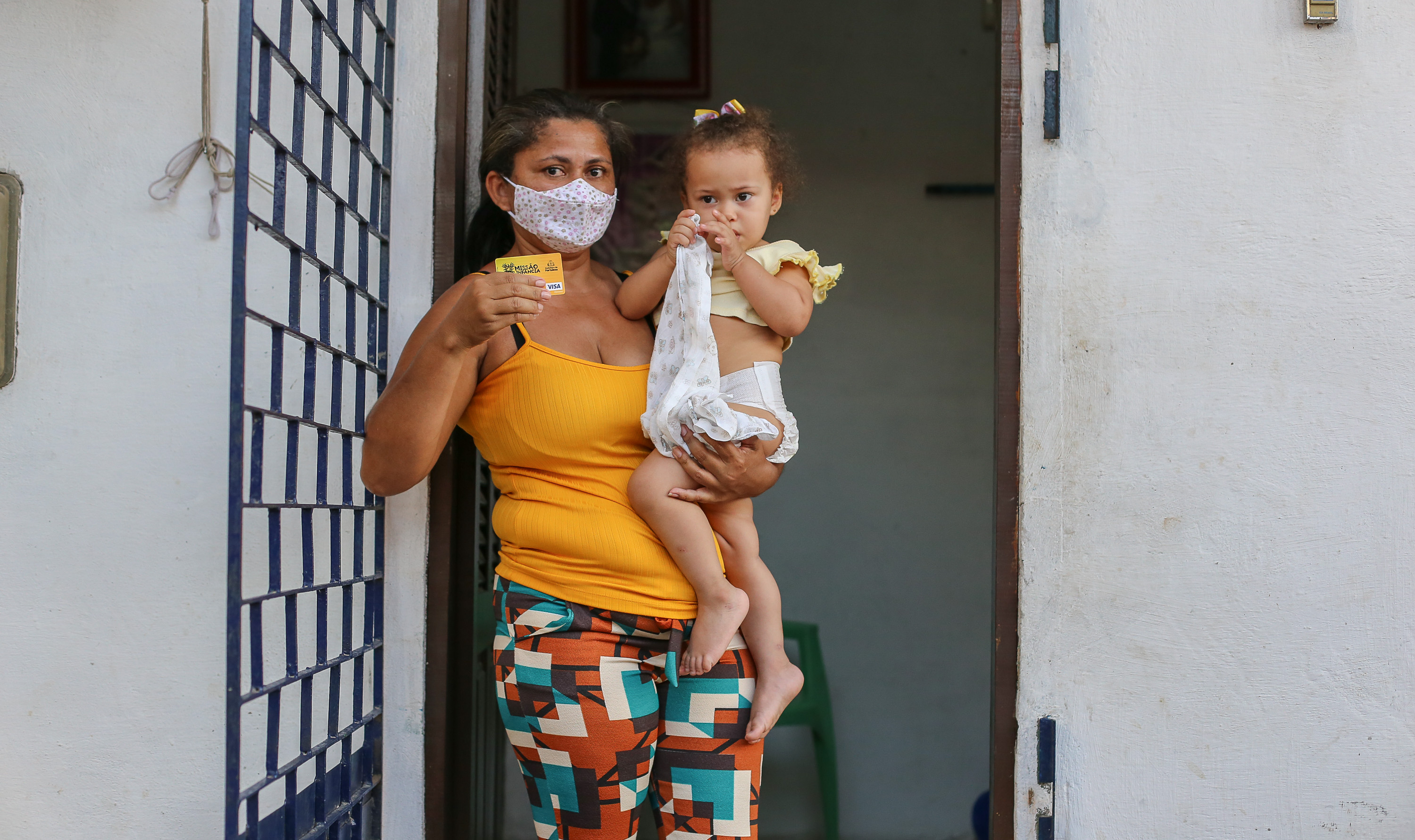 mulher segura a filha  no colo e mostra o cartão mais infância